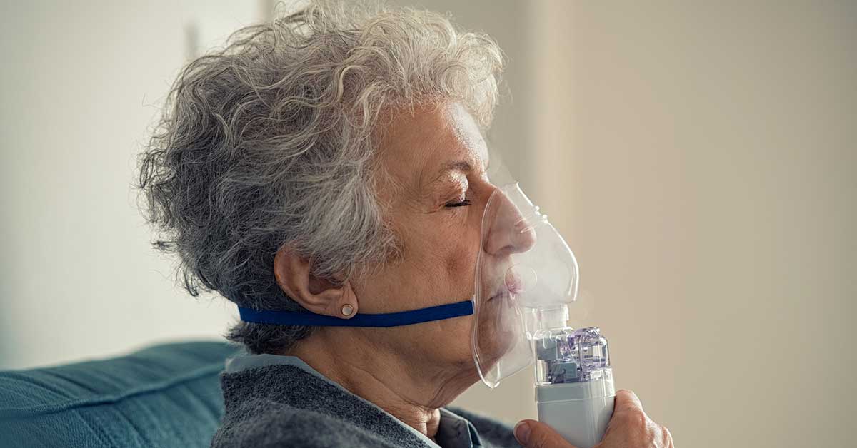 Sick senior woman making inhalation with nebulizer